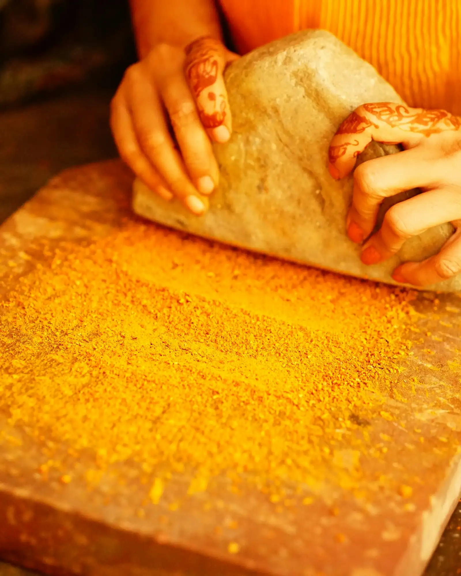 Hands with henna grinding turmeric on a stone slab