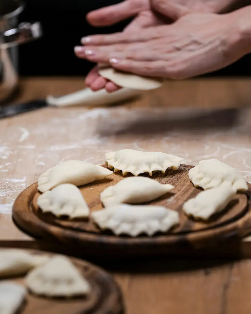 Hands pleating dumplings on a floured wooden board, finished dumplings lined up beside them