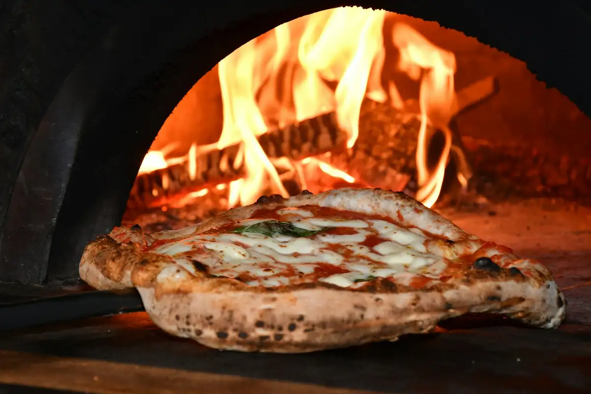 A pizza on a peel in front of the deck oven’s flames