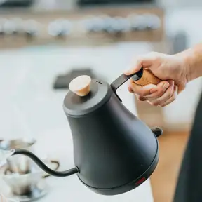 A hand pouring from a black gooseneck kettle over a pour-over cone