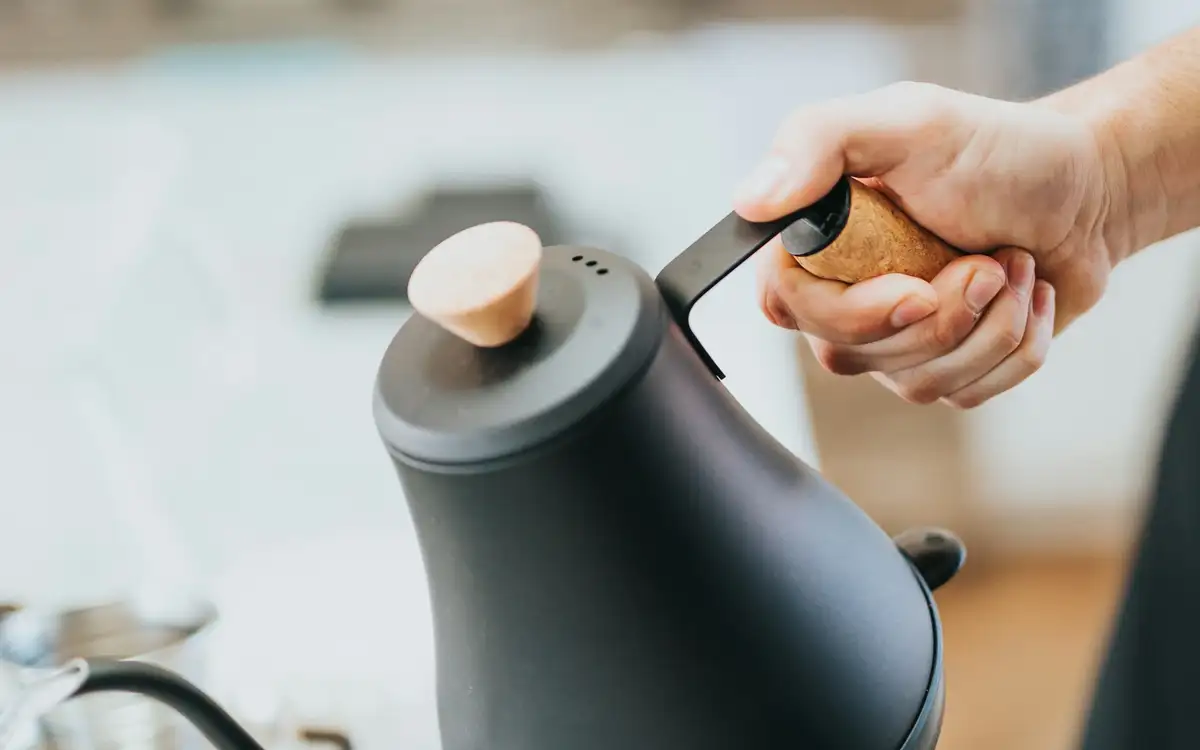 A hand pouring from a black gooseneck kettle over a pour-over cone