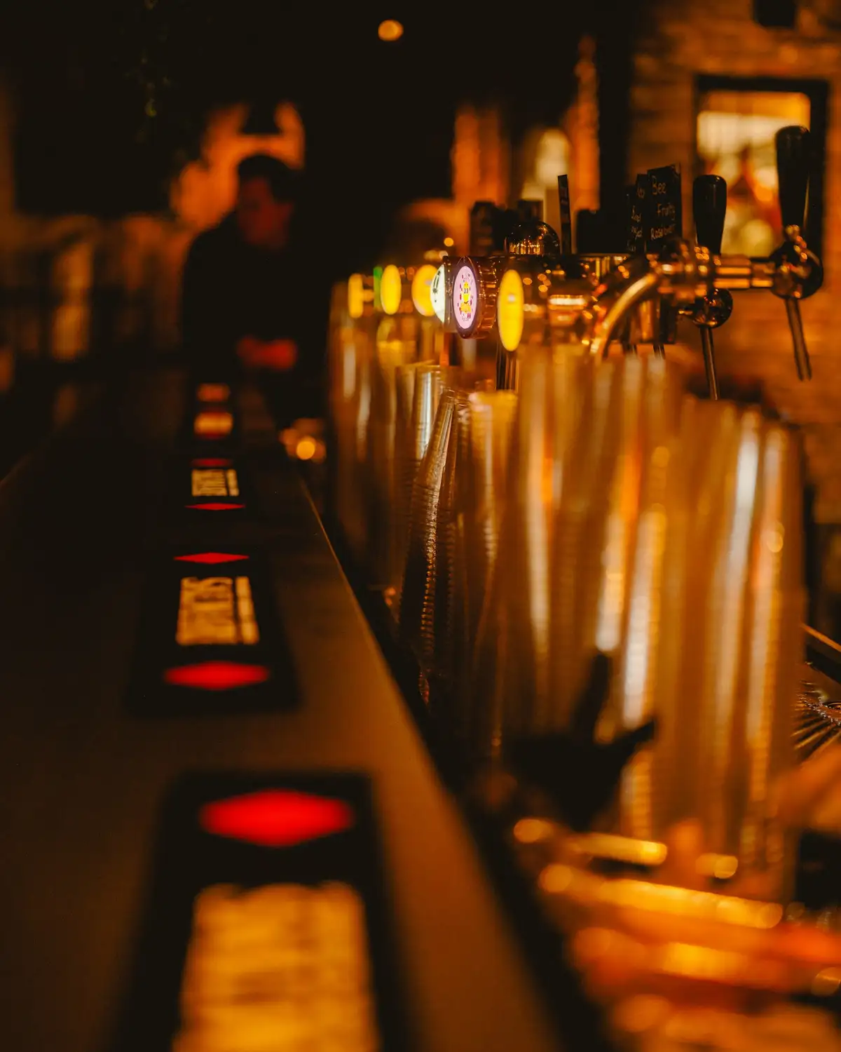 A row of beer taps along a dark bar, lit warm